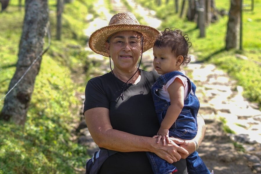 Una abuela con sombrero de paja carga a un niño pequeño en un sendero rural de Las Nubes, Costa Rica