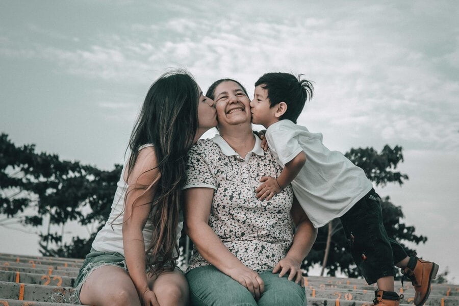 Una joven y un niño besan en la mejilla a una mujer mayor sonriente en Guayaquil, Ecuador