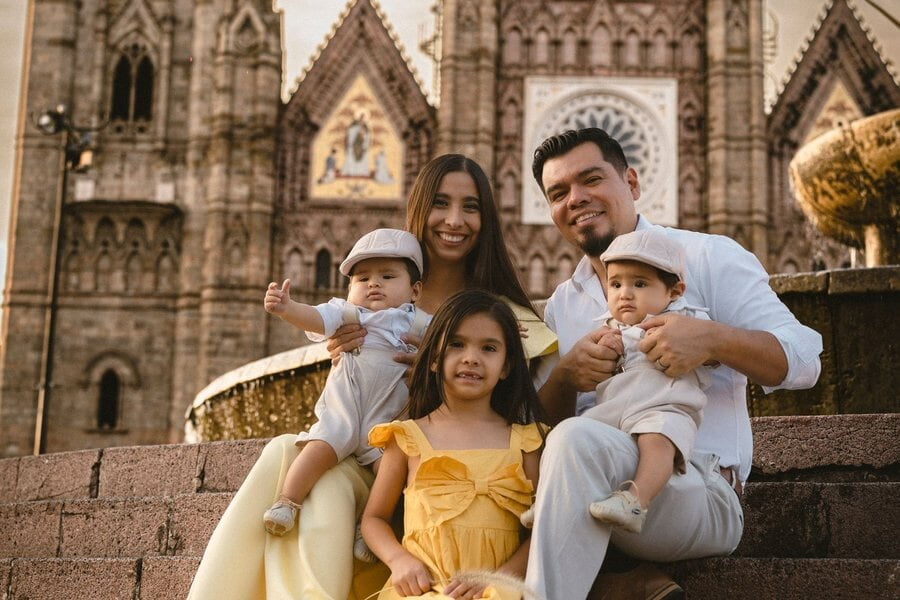 Una familia con tres niños pequeños sonríe sentada en las escalinatas del Templo Expiatorio de Guadalajara