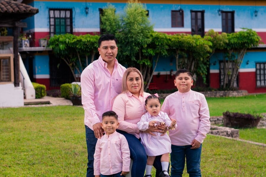Una familia de cinco con ropa a juego posa sobre el césped frente a una casa de estilo colonial