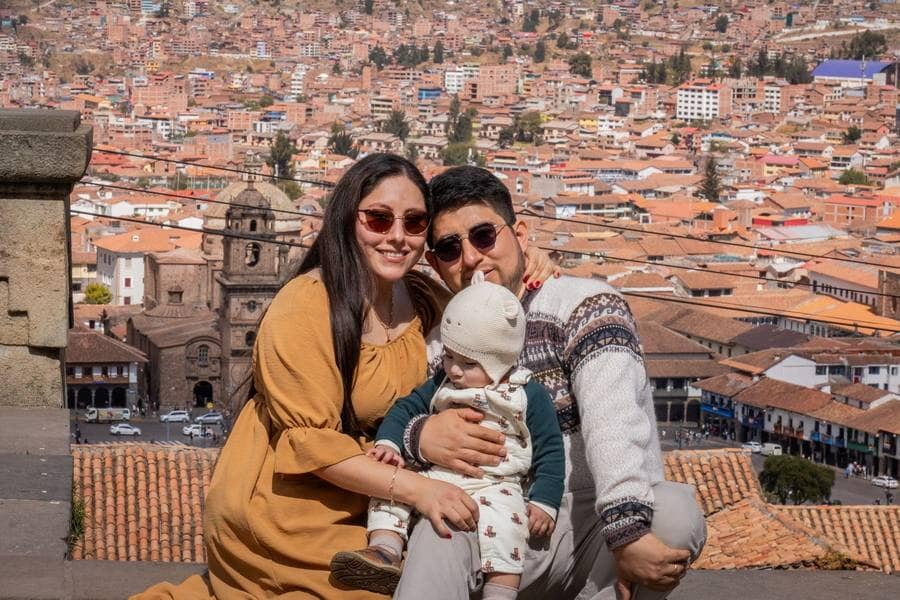 Una pareja con su bebé sonríe en un mirador con vista a la ciudad de Cusco