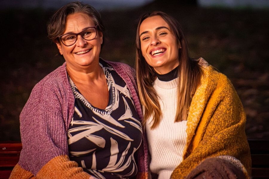 Una madre y su hija ríen sentadas en un banco de un parque al atardecer